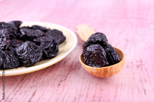 Bowl and spoon of prunes on color wooden background