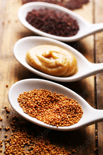 Mustard seeds, powder and sauce in spoons on wooden background