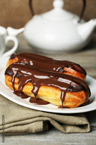Tasty eclairs and pot of tea on wooden table
