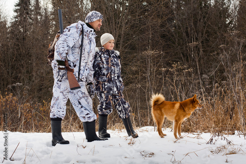 the hunter with his son and their dog on winter hunting