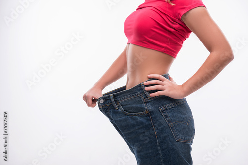Slim waist of young woman in big jeans showing successful weight