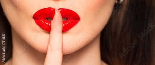 macro of lips with red lipstick finger showing hush and silence