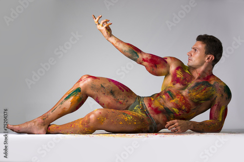 Schilderij op canvas Muscular man, skin painted with Holi colors, laying on the floor