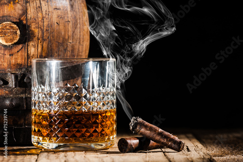Canvas Print Glass of alcohol and smoking noble cigar on a black background