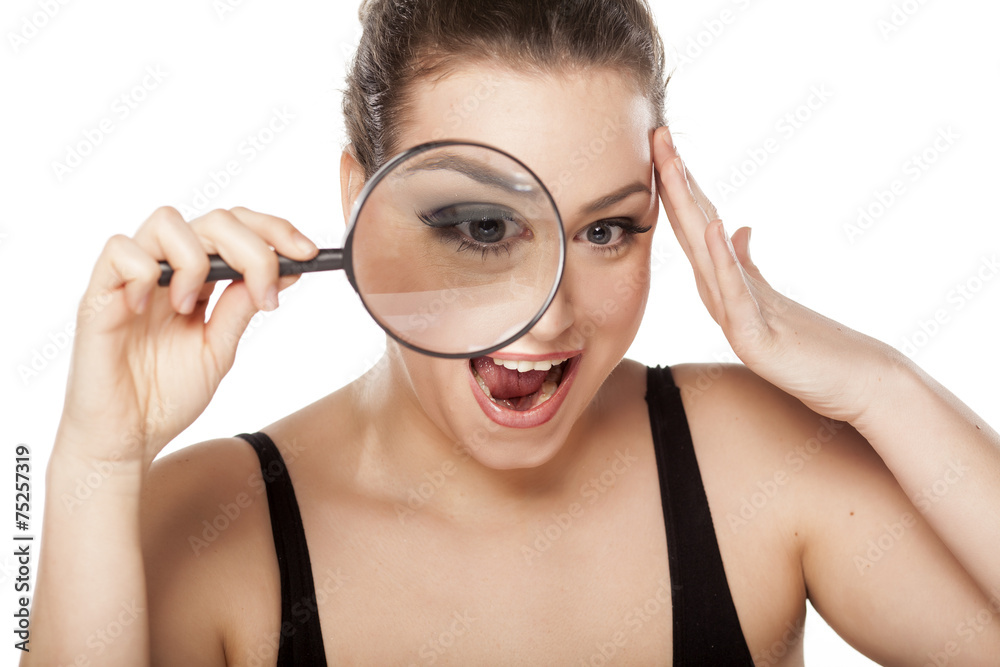 shocked young woman looking through a magnifying glass shocked young woman looking through a magnifying glass