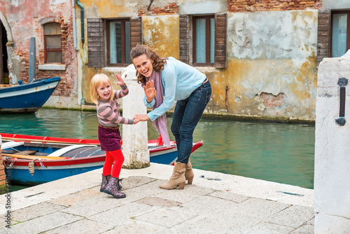 Happy mother and baby girl waving while walking in venice, italy