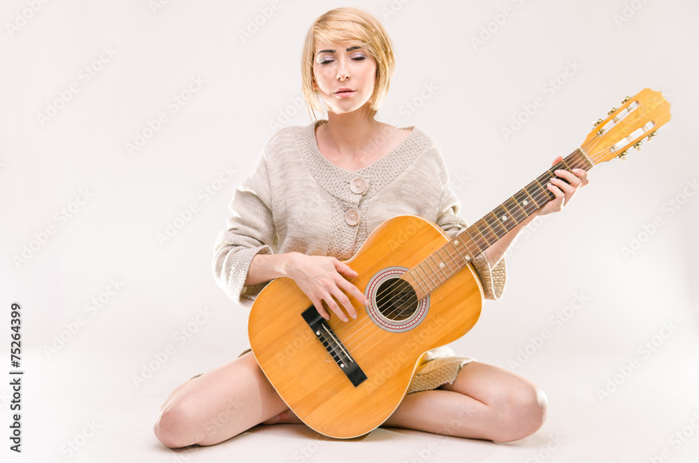 Fototapeta premium Young beautiful smiling blonde lady in sweater playing guitar