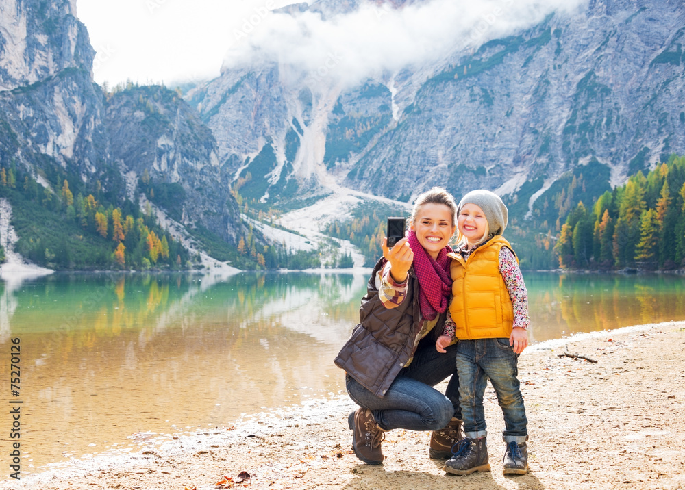 Happy mother and baby taking self photo on lake braies in italy