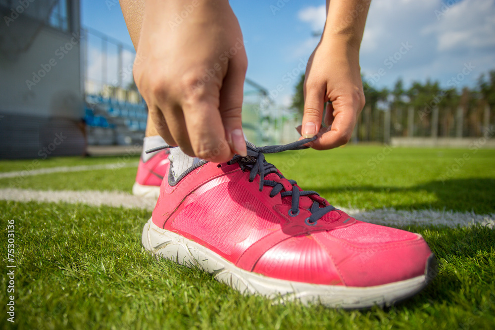 woman tying up pink sneakers on soccer field woman tying up pink sneakers on soccer field