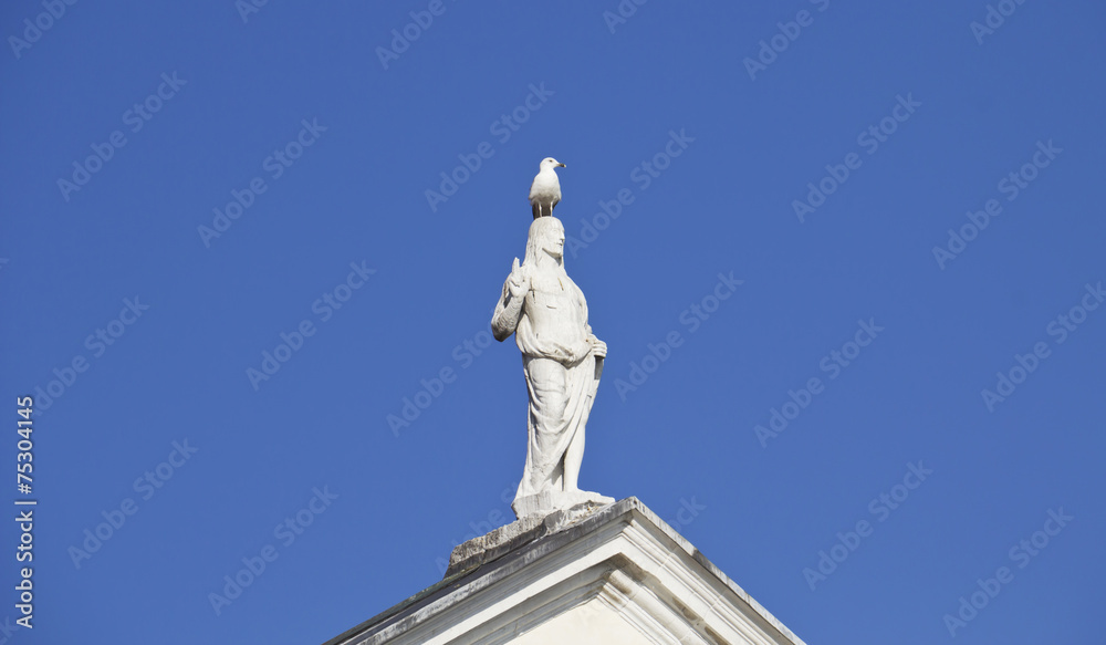 Statue of Jesus Christ on the deep blue sky background with a seagull on him