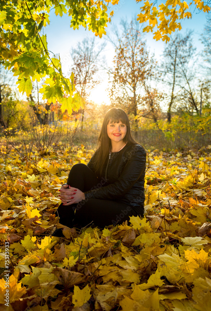 brunette woman sitting on grass at autumn park at sunny day brunette woman sitting on grass at autumn park at sunny day