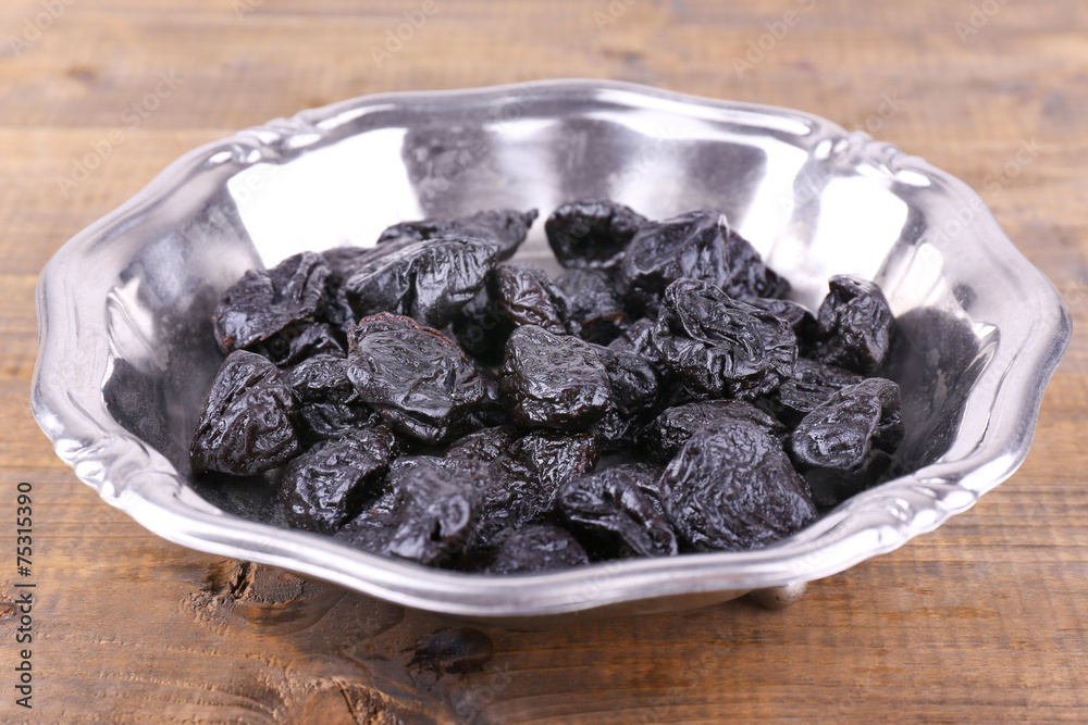 Metal plate of prunes on wooden background Metal plate of prunes on wooden background