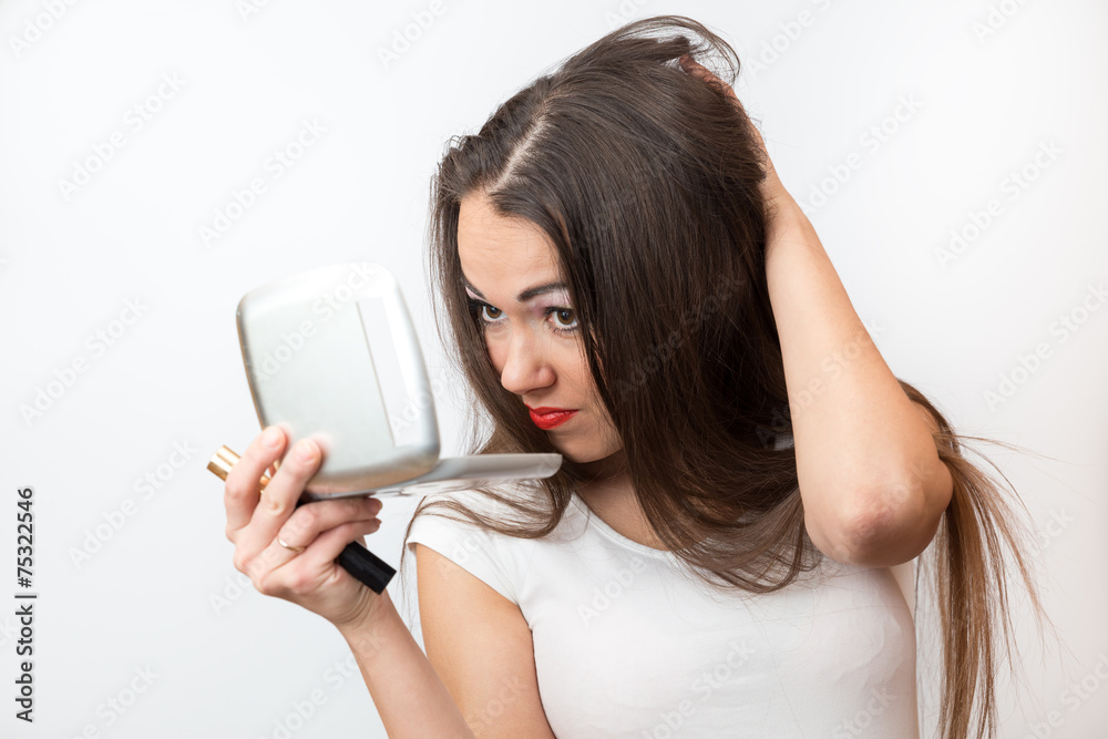 Brunette dissatisfied looks in the mirror doing her hair Brunette dissatisfied looks in the mirror doing her hair