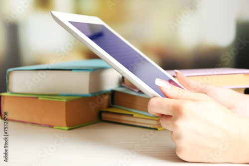 Female hand holding PC tablet near books, close-up. Modern