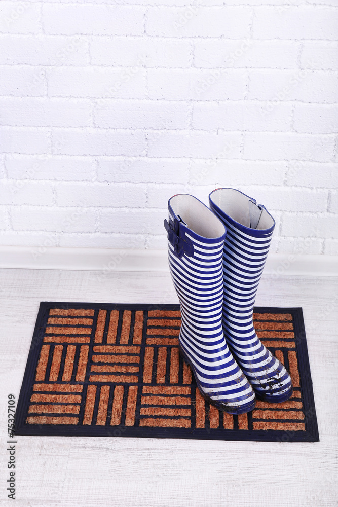 Naklejka premium Dirty wellington boots on door mat in room