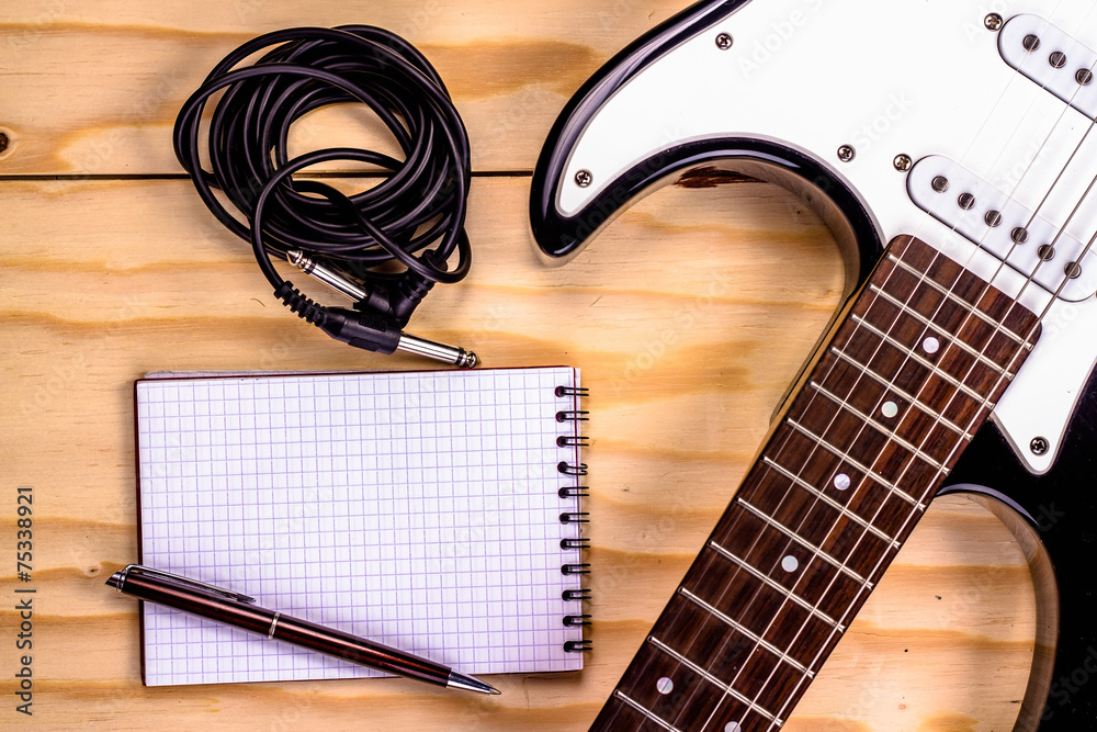 Naklejka premium open notebook with electric guitar on wooden background