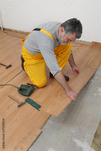 Adult male worker installing laminate floor,  floating wood tile