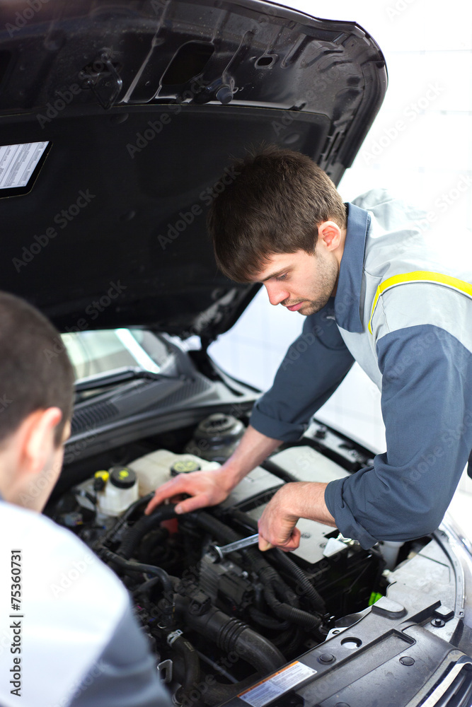 Two auto mechanics examining car with open hood Two auto mechanics examining car with open hood