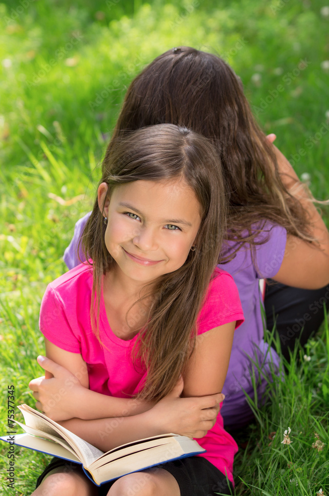 Smiling Girls reading book in the green gras Smiling Girls reading book in the green gras