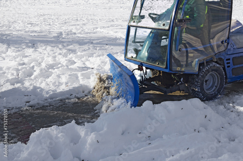 Blue snowplow removing snow from sidewalk and sprinkled salt antifreeze