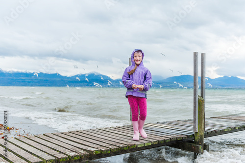 Little girl feeding birds by the lake on a very windy day photo