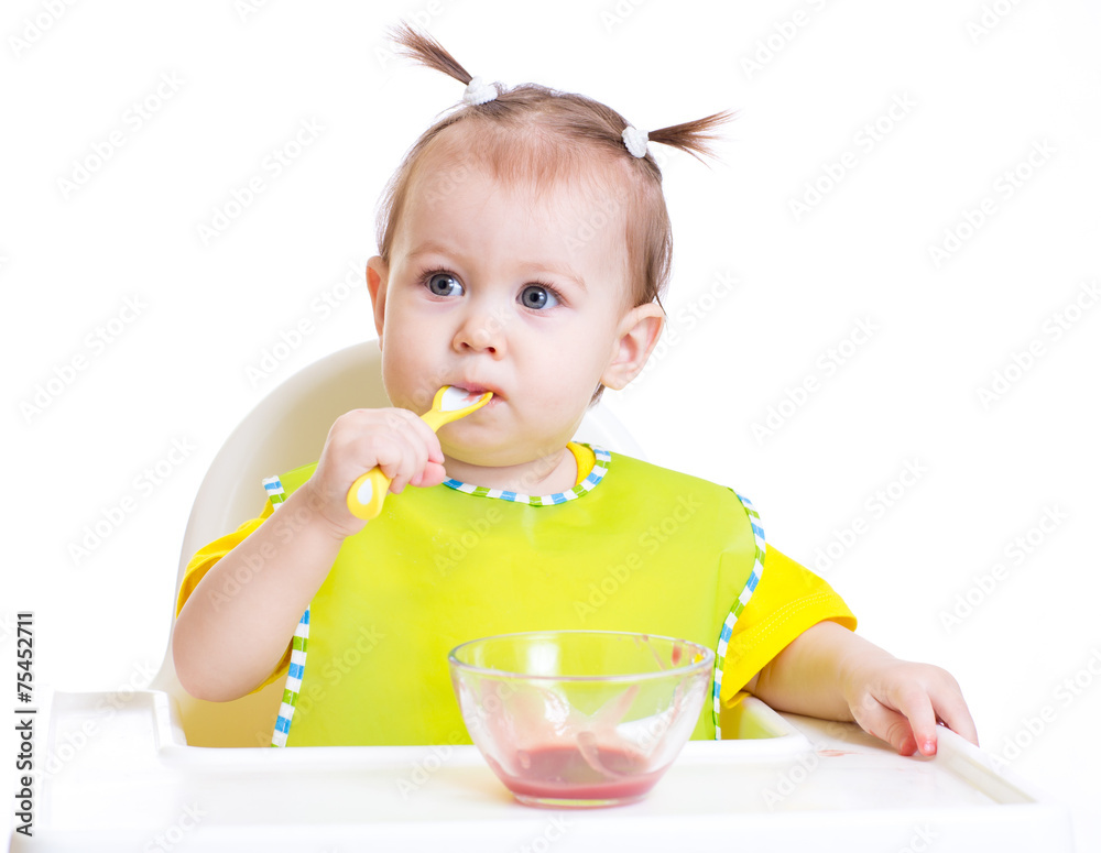 Baby eating with spoon sitting at table Baby eating with spoon sitting at table