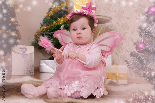 Baby girl with pink butterfly wings sitting under Christmas tree