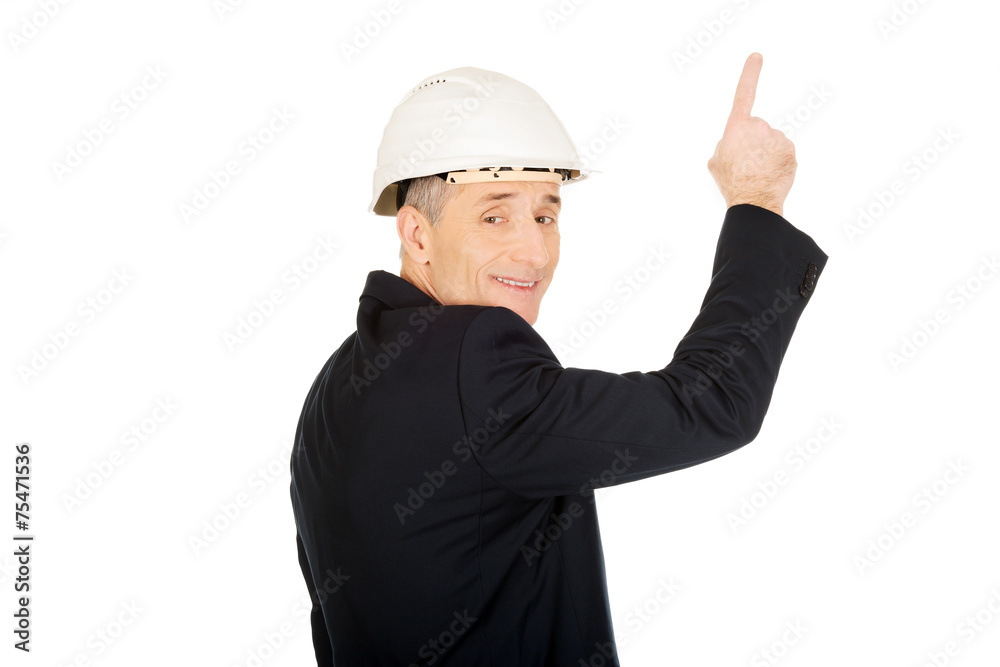 Smiling businessman with hard hat pointing up Smiling businessman with hard hat pointing up