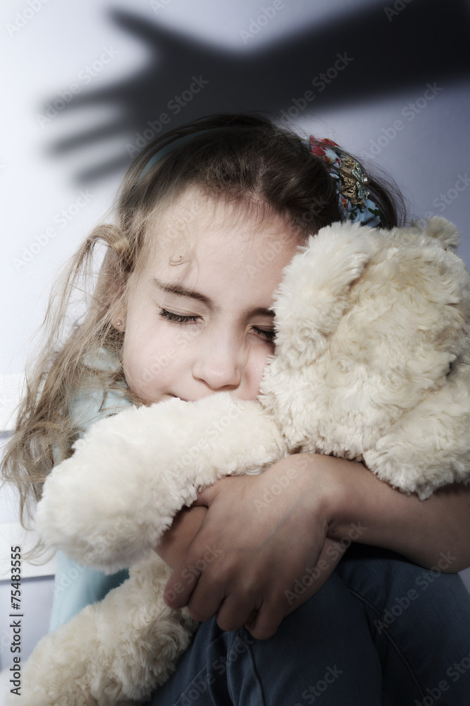 Troubled child sits huddled with teddy bear Troubled child sits huddled with teddy bear