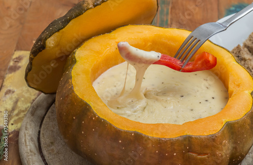 Cheese fondue in a roasted pumpkin with pepper on a fork