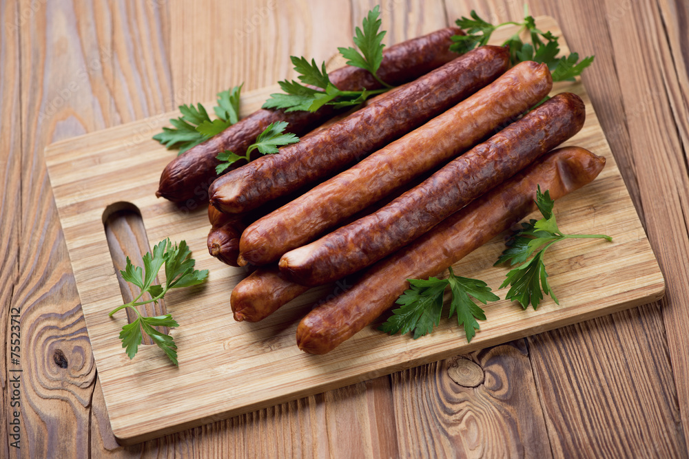 Wooden chopping board with smoked sausages and parsley