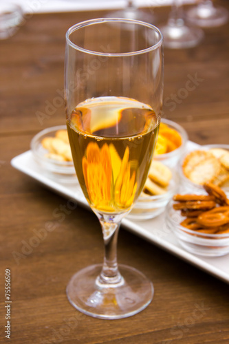 Flute with aperitif and pretzels on wooden table seen close