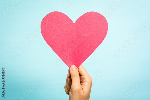 Hand holding red paper love heart shape on blue background.