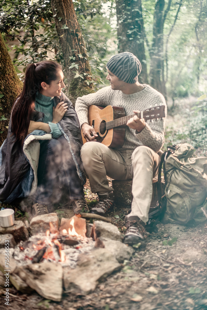 a couple sitting near a campfire, he plays guitar a couple sitting near a campfire, he plays guitar