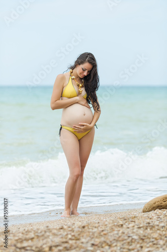 Pregnant woman in yellow bikini posing on the beach