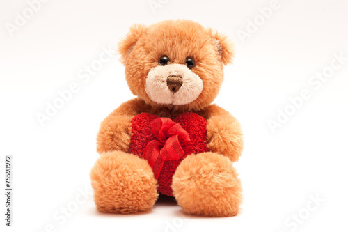 Isolated teddy bear holding a heart with a ribbon.