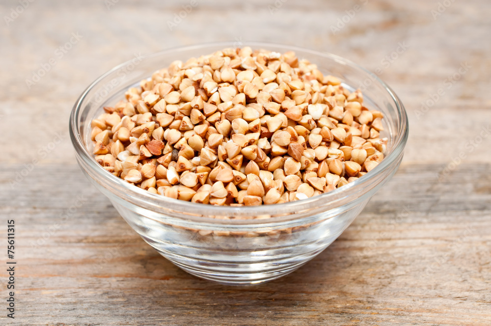 Dry buckwheat groats in a bowl on wooden table Dry buckwheat groats in a bowl on wooden table