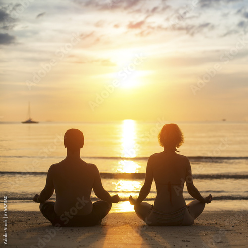Young yoga couple is meditating on the sea beach .