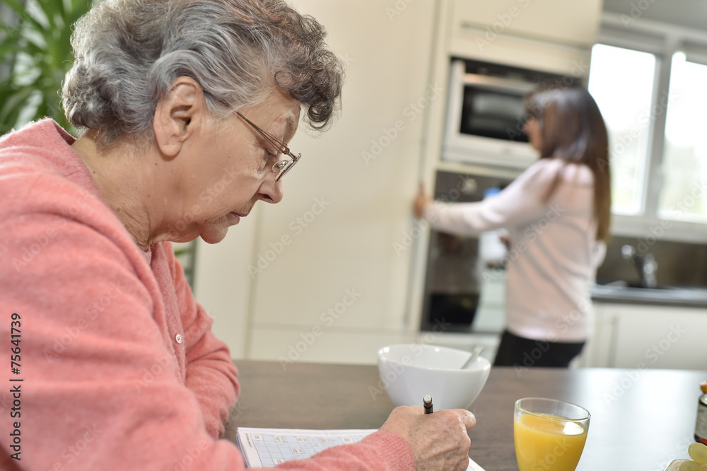 Elderly woman doing crosswords while homecare helps at home Elderly woman doing crosswords while homecare helps at home
