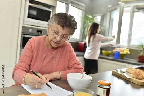 Elderly woman doing crosswords while homecare helps at home