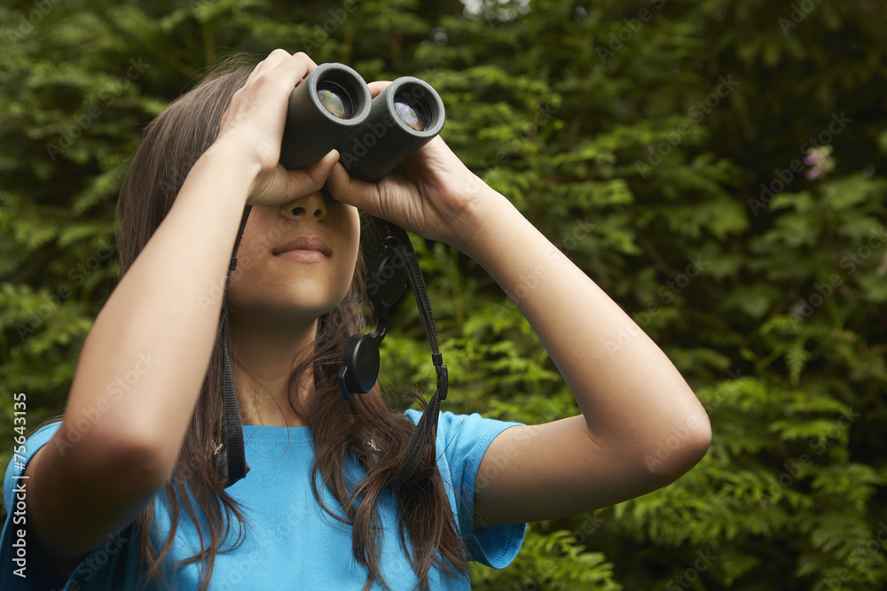 Girl looking through binoculars in forest