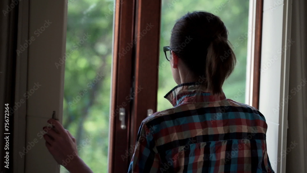 Woman opening shutter door and looking at trees from balcony Woman opening shutter door and looking at trees from balcony