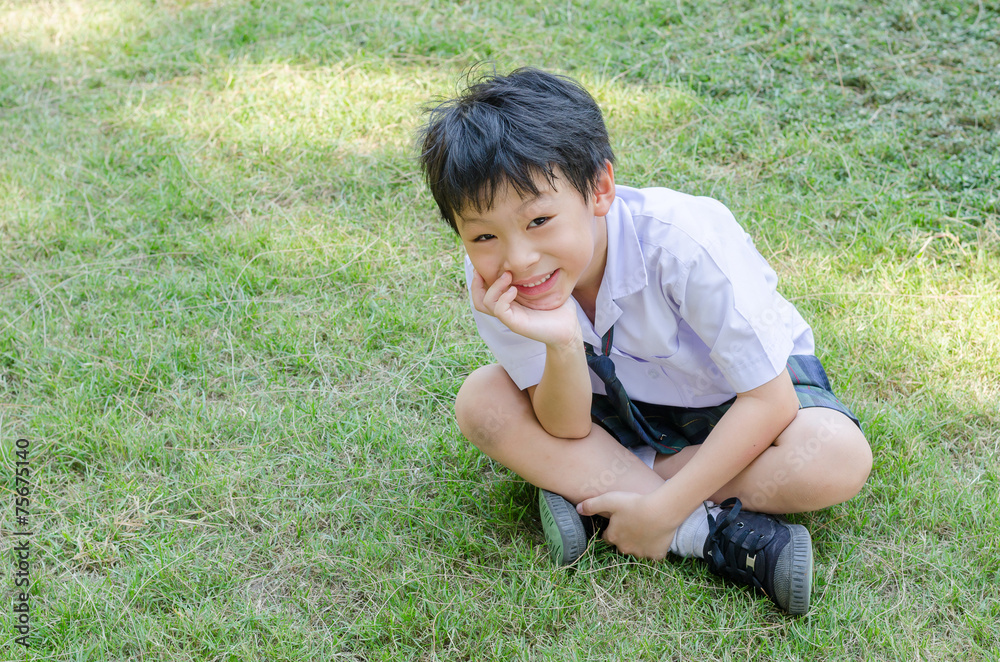 Happy Asian student sitting on grass field