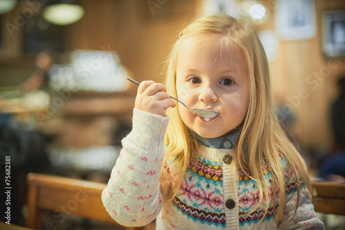 Little blond girl in a cafe drinking hot milk