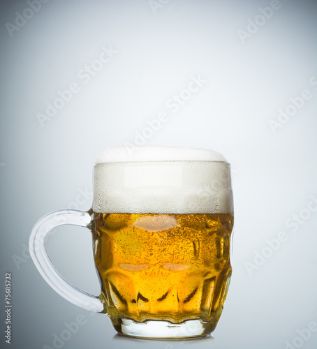 Mug with fresh beer and cap of foam on white background