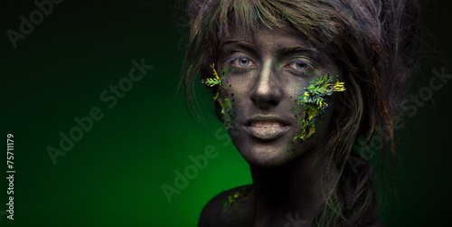 Fototapeta Naklejka Na Ścianę i Meble -  close-up portrait of woman in black paint and green leaf on face
