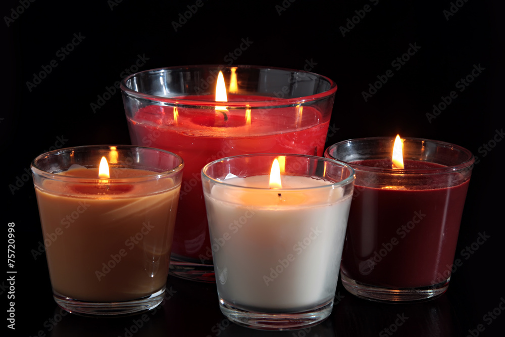Four of burning candles in glass candle holders on black Four of burning candles in glass candle holders on black