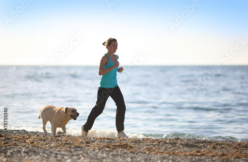 Woman running on the beach with dog. Outdoor workout fitness.
