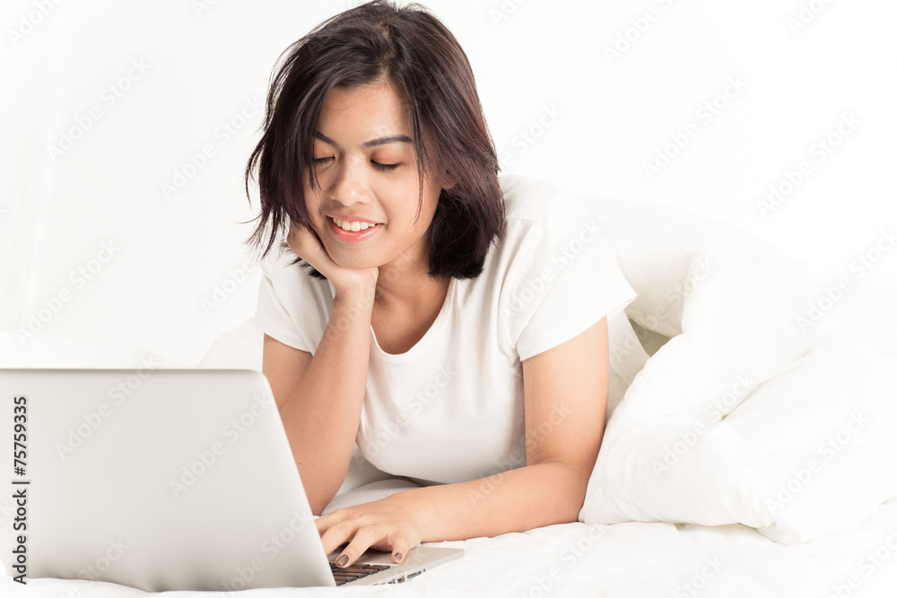 Smiling woman using a laptop while lying on her bed Smiling woman using a laptop while lying on her bed