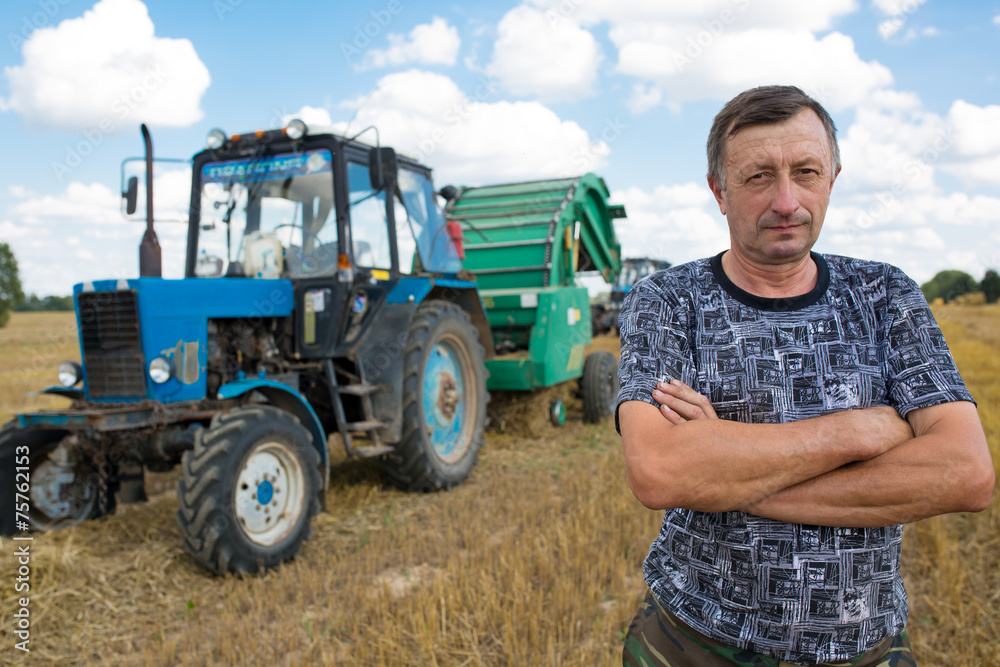Farmer standing in front of tractor hay bale maker farm machine Farmer standing in front of tractor hay bale maker farm machine